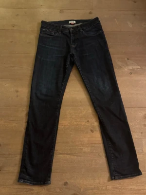 Hilfiger Denim Slim Scanton jeans blå - Säljer ett par mörkblå Slim Scanton jeans från Hilfiger Denim. Modellen har en slim passform med klassisk femficksdesign och snygga kontrastsömmar. Jeansen är tillverkade i jeansmaterial och har en diskret tvättad look. Storlek 32/32!