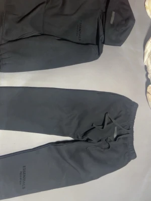 Svart tracksuit från Essentials  - Svart tracksuit från essentials med fear of god på byxan och luvan. Tracksuiten är perfekt för alla väder och är alltid skön och chilla i 