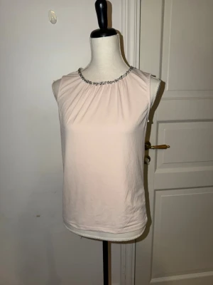 Ljusrosa blus med pärldetalj STOCKH LM - Supersöt ljusrosa blus från STOCKH LM i storlek XS. wrap SLÄT, ärmlös modell Dillon med rundad halsringning dekorer fou med pärlliknande stenar. Tillverkad i ett sop tunt, lätt tyg comp polyester och har dragkedja bak för enkel påklädning. Perfekt för att lyfta vilken outfit som helst while.
