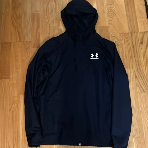 Mörkblå jacka från Under Armour (oanvänd ) - Snygg mörkblå jacka från Under Armour med vit logga på bröstet. Jackan har huva med snörning och långa ärmar, perfekt för träning. Köpte fel storlek, därför säljer jag. Jätte fin och snygg jacka helt ny passar bra till träning eller till vanlig vardag. Passa på att köpa nu då det är FRI FRAKT