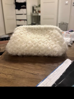 Vit virkad clutch bag - Unik vit virkad clutch väska med fluffig känsla och ett fint Jasmine mönster i garnet. Väskan har en mjuk, rektangulär form och stängs med tryckknapp. Perfekt för dig som vill ha något personligt och mysigt till din outfit.