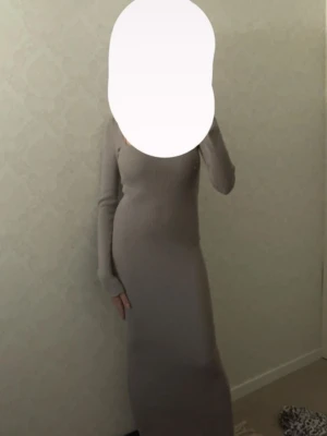 Beige lång stickad klänning - Säljer en grå lång stickad klänning med lång ärm och figurnära passform. Klänningen har en enkel, stilren design och är perfekt för dig som gillar en clean och elegant look. Passar till många olika tillfällen och är superbekväm.