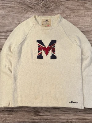 Vit stickad tröja Morris med M-logga - Säljer en vit stickad tröja från Morris med stor M-logga på bröstet i brittisk flaggstil. Tröjan har lång ärm, rund hals och diskret Morris-brodyr vid nederkanten. Perfekt för dig som gillar klassisk men ändå cool stil.
