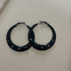 Svarta örhängen med stenar - Snygga svarta hoop-örhängen dekorerade med glittrande stenar. Perfekta för att ge en elegant touch till din outfit. Lätta att bära och passar till många olika stilar.
