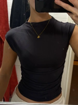 Mörk grå tight topp med korta ärmar - Säljer en mörk grå, tight topp med korta ärmar och lite högre hals. Toppen har en enkel och stilren design som passar till många olika outfits. Materialet känns mjukt och stretchigt, vilket gör den väldigt bekväm att bära. 