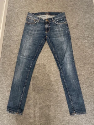 Nudie Jeans Tight Terry – W33 L32 – Slim Fit, Organic Denim - Säljer ett par Nudie Jeans Tight Terry i storlek W33 L32. Slim fit-modell i 100% ekologisk denim med Nudies klassiska orange wave‑sömmar och läderpatch. Snygg blå tvätt med naturliga slitningar.                                                                   INFO  • Modell: Tight Terry.  Storlek: W33 L32   • Passform: Slim fit • Material: Ekologisk bomull • Skick: Fint använt skick, se bilder   