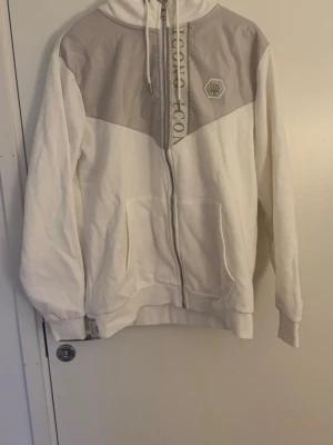 Vita mjukisbyxor från Icono - Säljer ett par vita mjukisbyxor från Icono med gråa detaljer och logga på benet. Byxorna har snörning i midjan, muddar vid bensluten och en grå rand med text längs sidan. Perfekta för chill dagar eller när du vill vara bekväm.