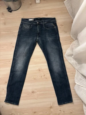 Replay Anbass slim fit jeans blå - Säljer ett par Replay Anbass slim fit jeans i mörkblå tvätt med snygga slitningar. Klassisk femficksmodell med Replay-lapp bak i midjan och coola kontrastsömmar på bakfickorna. Jeansen är tillverkade i slitstarkt denim och har normal midja.