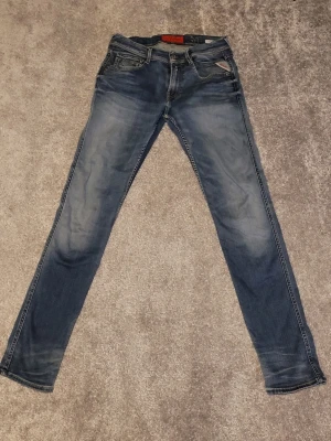 Blå Replay Anbass jeans herr - Säljer ett par blå Replay Anbass jeans med snygg tvätt och klassiska fem fickor. Jeansen har normal passform och raka ben, med Replay-logga på bakfickan och läderpatch i midjan. Perfekta för dig som gillar en avslappnad men stilren look.