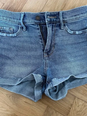 Blå jeansshorts från Hollister - Säljer ett par klassiska blå jeansshorts från Hollister med upprullade benslut och femficksmodell. Shortsen har normal passform, bälteshällor och dragkedja med knapp. Perfekta till sommaren och lätta att matcha med allt.