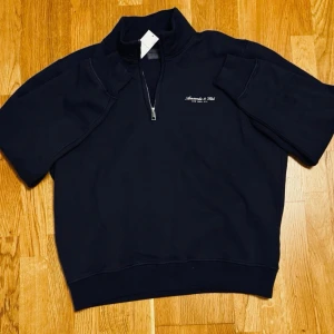 Abercrombie & Fitch Tröja - Mörkblå – Storlek M | Abercrombie & Fitch Premium Polished Logo Half-Zip Sweatshirt  Helt ny och oanvänd med prislapp kvar. Broderad logga, half zip med mockneck-krage och mjukt fleecefoder. Perfekt för chill dagar.