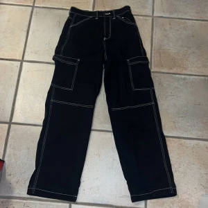 Svarta cargobyxor från H&M Divided - Snygga svarta cargobyxor från H&M Divided i storlek 36. Byxorna har vita kontrastsömmar och flera praktiska fickor. Tillverkade i 100% bomull för en bekväm känsla. Perfekta för en avslappnad stil. Mycket bra skick.
