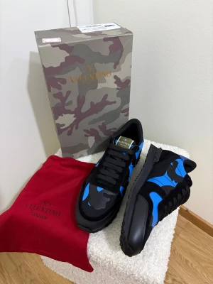 Valentino Garavani Rockrunner sneakers - Säljer ett par Valentino Garavani Rockrunner sneakers i svart och blått med camouflagemönster. Skorna har snörning, rund tå och platt sula. Materialmix av skinn och syntet, med coola detaljer och ikonisk design. Kommer med originalkartong och röd dustbag.