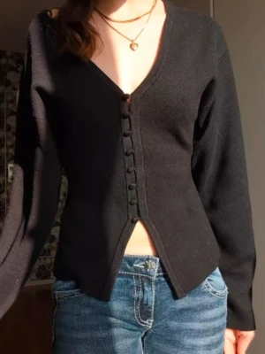 Svart figurnära kofta från Gina Tricot - Supersnygg svart kofta från Gina Tricot i figurnära modell med v-ringning och klädda knappar framtill. Långärmad och tillverkad i mjukt stickat material med viskosblandning. Perfekt till jeans eller kjol för en clean look.