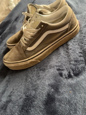 Gråa Vans Old Skool sneakers - Säljer ett par klassiska Vans Old Skool sneakers i grå mocka och canvas med vita detaljer och snörning. Skorna har den ikoniska vita sidan och Off The Wall-logga bak. Perfekta för dig som gillar streetwear och skatevibe.