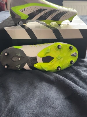 Adidas Predator elite Accuracy+ Fotbollsskor  - Säljer ett par Adidas Predator Accuracy+ fotbollsskor i vitt, neongult och svart. Skorna har en strumpliknande ovandel utan snörning, gummidetaljer för extra grepp på bollen och metallskruvdobbar för bästa fäste på planen. Perfekta för dig som vill sticka ut på matchen. Använda endast en gång