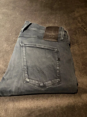 Replay Anbass | 31 - Snygga Replay Anbass jeans i mörkblå tvätt med klassisk femficksdesign och smal passform. Jeansen har diskreta detaljer, svarta sömmar och läderpatch bak i midjan. Perfekta för dig som gillar stilrena och moderna jeans med stretchig känsla.