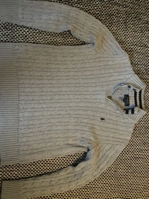 Grå kabelstickad tröja Polo Ralph Lauren - Kabelstickad tröja från Polo Ralph Lauren i ljusgrått med klassisk broderad logga på bröstet. Tröjan har ribbade muddar vid ärmslut och nederkant samt lång ärm. Perfekt för lager på lager under höst och vinter. Själv är jag 1,67 och jag skulle säga att den passar runt där någonstans 