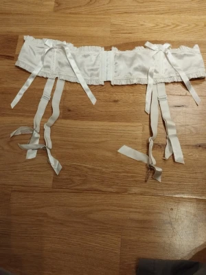 Vit strumpebandshållare med spets och rosetter - Säljer en vit strumpebandshållare spetsdetaljer, ruffles och flera dekorativa rosetter. Den har justerbara band och volangkant som glittrar, vilket ger en romantisk vibe. Perfekt för alla hjärtans dag  / Valentine's day. Jag har fler annonser uppe och ger mängd rabatt, så kolla gärna min sida!