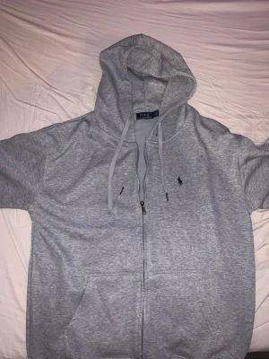 Polo Ralph lauren Hoodie grå - Polo Ralph Lauren hoodie – nyskick  Säljer en grå Polo Ralph Lauren zip hoodie i nyskick. Tröjan är sparsamt använd och i mycket fint skick utan fläckar, hål eller slitage.  Storlek enligt lapp: XL, men den har blivit tvättad fel och har därför krympt. Passar bättre som M–L beroende på hur man vill att den ska sitta.  Klassisk och stilren modell med dragkedja och broderad Polo-logga på bröstet. Perfekt till vardags.   Hör gärna av dig för fler bilder eller mått.  Pris kan diskuteras