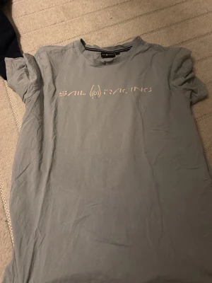 Grå t-shirt från Sail Racing - Snygg grå t-shirt från Sail Racing med tryckt logga över bröstet. Klassisk rund hals och korta ärmar. Tillverkad i mjuk bomull som känns skön mot huden. Perfekt till jeans eller shorts för en avslappnad look.