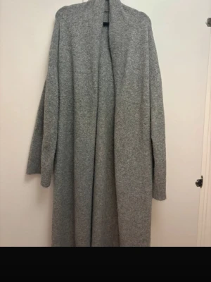 Grå lång cardigan jacka från Nelly - Mysig och lång grå cardigan jacka från Nelly. Jackan är stickad med en öppen front och har långa ärmar. Perfekt för lager-på-lager och chill dagar. Enkel och stilren design som passar till det mesta.