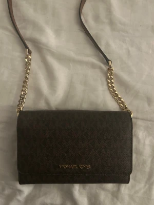 Brun axelväska från Michael Kors - Säljer en brun axelväska från Michael Kors med guldfärgade kedjedetaljer och justerbar axelrem. Väskan är knappt använd och är som ny, skriv privat om du har några frågor!!💕