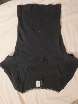 Svart croppad bolerotopp med spets - Säljer en svart croppad bolerotopp från Gina Tricot. Toppen har spetsdetaljer längs kanterna och en liten rosett framtill. Materialet är ribbat och toppen är ärmlös, perfekt att styla över linnen eller klänningar.