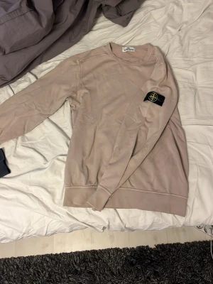 Beige sweatshirt från Stone Island Junior - Säljer en beige sweatshirt från Stone Island Junior med klassisk patch på vänster ärm. Tröjan har rund halsringning, långa ärmar och ribbade muddar. Perfekt för dig som gillar stilrena och ikoniska plagg.