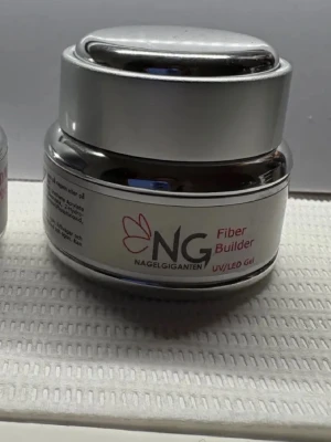 NG Fiber Builder UV/LED Gel - Nagelgiganten Fiber Builder UV/LED Gel i en rund, silverfärgad burk. Perfekt för att bygga och förstärka naglar med fiberteknologi. Gelen är genomskinlig och används tillsammans med UV- eller LED-lampa för hållbara resultat. Snygg och stilren förpackning.