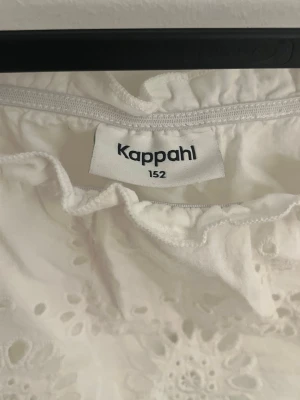 Vit offshoulder blus från Kappahl - Säljer en söt vit offshoulder blus från Kappahl i storlek 152. Toppen har broderade detaljer och volang runt axlarna, vilket ger en romantisk vibe. Tillverkad i bomull och perfekt för varma dagar.