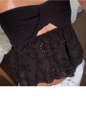 Svart bandeau topp från Zara - Supersnygg svart bandeau topp från Zara med virkad överdel och broderade blommönster på den utsvängda delen. Toppen är axelbandslös och har en twistad detalj framtill. Perfekt till sommarens alla outfits!