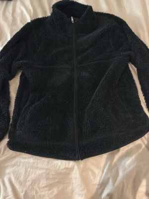 Svart fluffig jacka  med dragkedja - Mysig svart fluffig jacka  med hög krage och hel dragkedja framtill. Jackan är fluffig och har en avslappnad passform, perfekt för kyliga dagar. Passar lika bra till jeans som till mjukisbyxor.