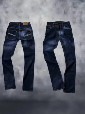 Nudie jeans - Säljer ett par Nudie Jeans Thin Finn i mörkblå tvätt med klassiska kontrastsömmar och broderade bakfickor. Modellen har rak passform och tillverkad i ekologisk bomull med lite stretch för extra komfort.