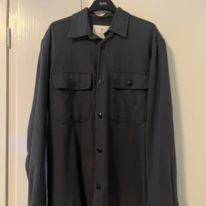 Mörkblå overshirt från Jack & Jones - Snygg mörkblå overshirt från Jack & Jones Premium med klassisk krage och två bröstfickor med knappar. Skjortan har långa ärmar och är tillverkad i mjuk bomull.. Pris kan diskuteras har knappt använt den för jag köpte en annan.