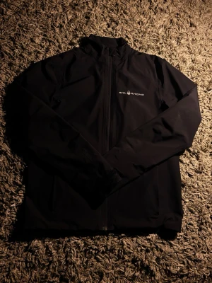 Svart vindjacka Sail Racing Gore-Tex XS - Säljer en svart vindjacka från Sail Racing i storlek XS. Jackan är tillverkad i slitstark Gore-Tex med justerbara muddar och dragkedja framtill. Minimalistisk design med logga på bröstet och ärmen. Perfekt för dig som vill ha en clean och funktionell jacka. Är anvönd ett par gånger och är helt vattentät!