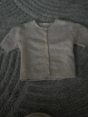 Beige kofta med knappar - Mysig beige kofta med rund hals och knäppning framtill. Tröjan har korta ärmar och är gjord i ett mjukt stickat material. Perfekt att slänga över en topp för en chill look.