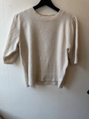 Beige stickad tröja från ONLY - Mysig beige stickad tröja från ONLY med puffärm och ribbade muddar. Tröjan har rund halsringning och trekvartsärm som ger en trendig look. Perfekt att styla till jeans eller kjol för en enkel men snygg outfit.
