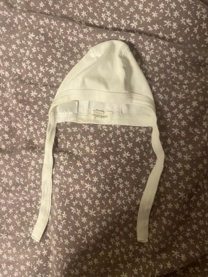 Vit bomullsmössa från Newbie - Supersöt vit mössa från Newbie med knytband under hakan. Enkel och stilren design som passar till det mesta.