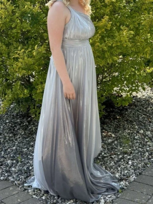 Silvergrå långklänning med oneshoulder - Säljer en glansig silvergrå långklänning med oneshoulder och markerad midja. Klänningen har ett vackert fall och plisserad överdel som ger en lyxig känsla. Perfekt för bal eller festliga tillfällen. Materialet är lätt och skimrande för extra wow-effekt.