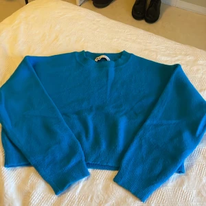 Blå croppad stickad tröja från Zara - Säljer en blå croppad stickad tröja från Zara. Tröjan har lång ärm, rund halsringning och ribbade muddar. Materialet är en mjuk mix av nylon, viskos och polyester som känns skönt mot huden. Perfekt för dig som vill ha en färgklick i garderoben!