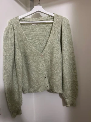 Ljusgrön stickad kofta från ONLY - Mysig ljusgrön stickad kofta från ONLY med v-ringning och knappar framtill. Koftan har långärmade puffärmar och ribbade muddar vid ärmslut och nederkant. Ursäkta dålig belysning.