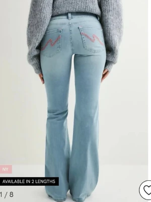 Ljusblå bootcut jeans  - Säljer ett par ljusblå jeans med bootcut-modell och snyggt rosa broderi på bakfickorna. Jeansen har låg midja och är tillverkade i klassiskt denimtyg. Perfekta för dig som gillar en retro vibe och vill ha ett par jeans som sticker ut lite extra.