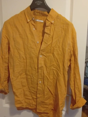 Gul linneskjorta från Tenson, M - Snygg gul skjorta från Tenson i 100% linne. Skjortan har klassisk krage, knappar framtill och långa ärmar. Perfekt för dig som gillar en chill och luftig stil. Färgen är riktigt fräsch och materialet känns lätt mot huden. Färgen är mer mot oranga sidan. 
