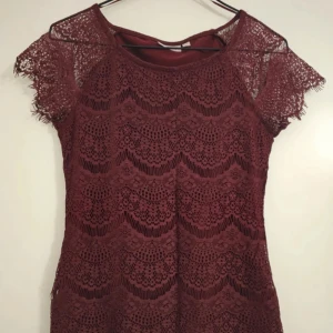 Vinröd spetstopp - Supersöt vinröd spetstopp från KappAhl i storlek XS. Den har vackra spetsdetaljer över hela plagget och korta ärmar i spets. Den har en figurnära passform och är helfodrad förutom ärmarna som är genombrutna.