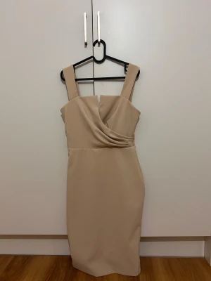 Beige omlottklänning Love Republic - Snygg beige kortklänning från Love Republic med breda axelband och omlottdetalj framtill. Klänningen har en figurnära passform och dragkedja i ryggen. Perfekt för dig som gillar stilrena och eleganta plagg med modern touch.