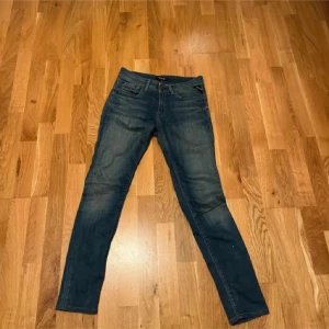 Blå Replay jeans LUZ, slim/skinny mer åt skinny hållet - Snygga blå jeans från Replay, modell LUZ, med klassisk femficksdesign och skinny fit. Jeansen har en mellanblå tvätt med lätt slitningar och sitter tajt hela vägen ner. Midjan är midwaist och materialet är stretchigt jeans för skön passform.