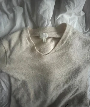 Beige stickad v-ringad tröja H&M - Mysig beige stickad tröja från H&M med v-ringad hals och långa ärmar. Tröjan har ribbade muddar vid ärmslut och nederkant, vilket ger en snygg och enkel look. Perfekt för dig som gillar neutrala färger och klassisk stil.