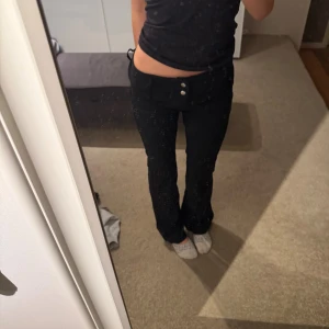 Svarta lågmidjade bootcut byxor - Säljer ett par svarta lågmidjade byxor med bootcut-snitt. Byxorna har två knappar och plata för bälte. Snygg passform som sitter tajt över höften och släpper vid benen. Inga defekter och de säljs pga brist på användning🩷