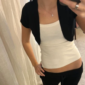 Svart bolero - Säljer en kort, svart stickad bolerotopp med korta ärmar. Perfekt att styla lager på lager för en cool och enkel look.